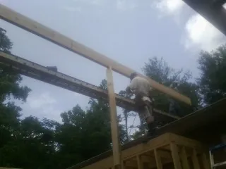Carpenter setting a ridge beam over a new addition frame in Flora