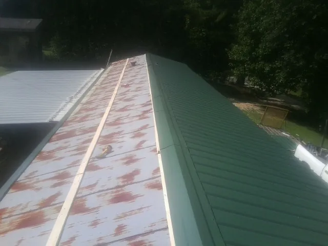 Old rusted panels beside newly installed green metal roofing — Wind Damage Roof Repair by Roofing Brothers in Flora