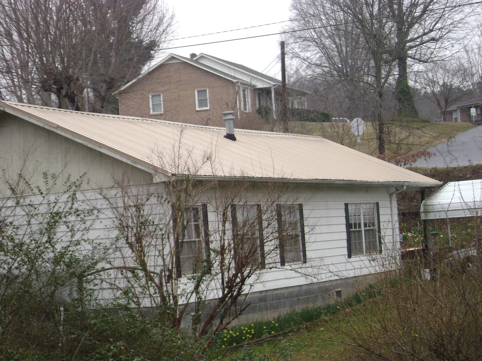 Tan metal roof on a white sided house set into a hillside — Commercial Roofing by Roofing Brothers in Flora