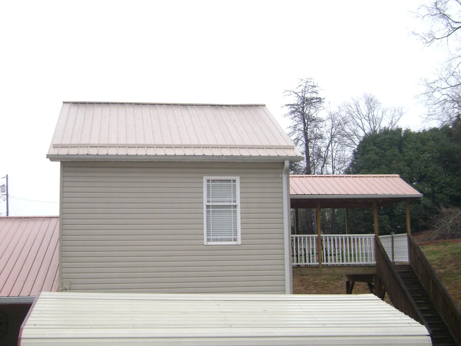 Tan metal roofs on a two story addition and attached porch, from a Roof Replacement job in Flora